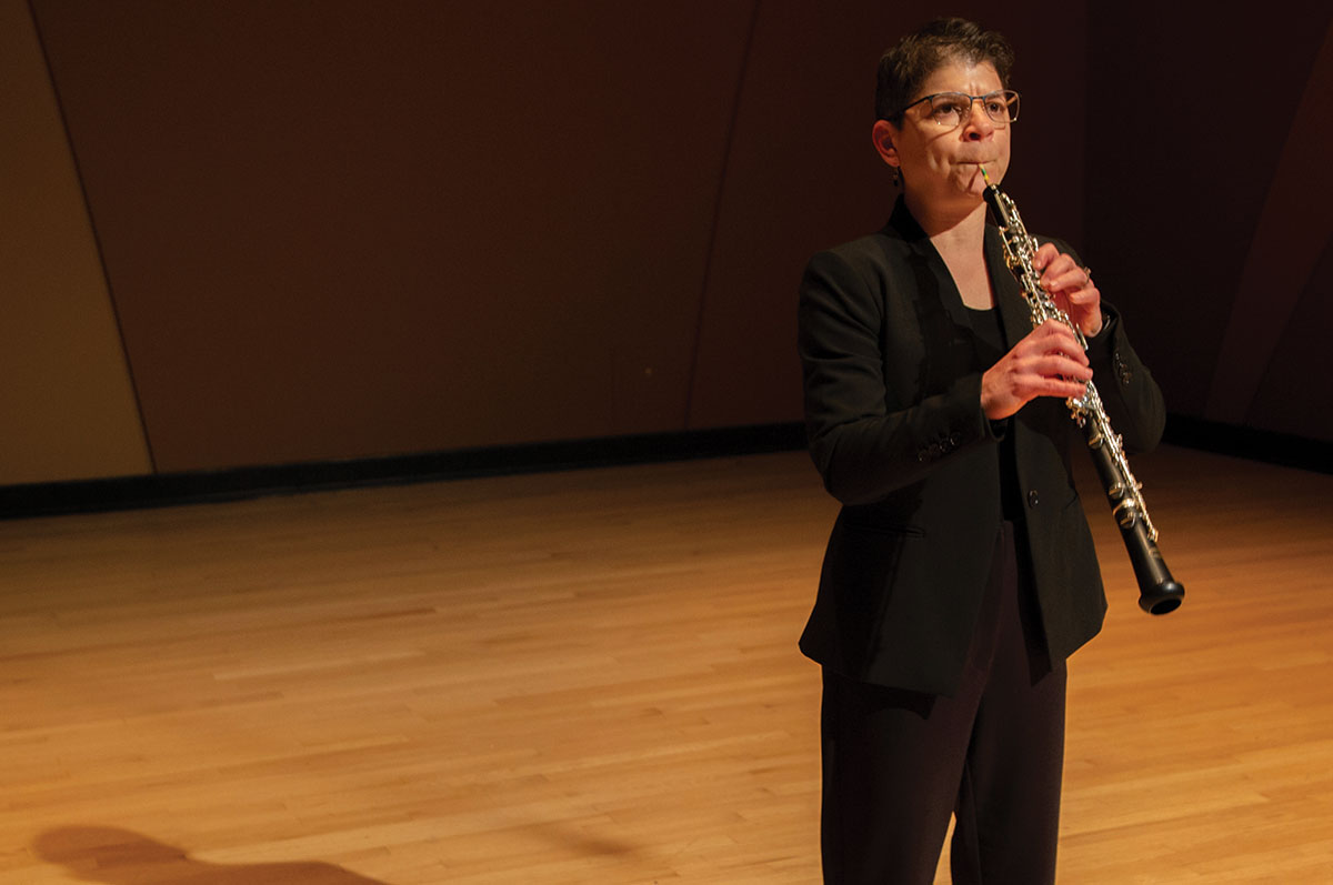 Miriam Kapner stands alone on a stage playing an oboe