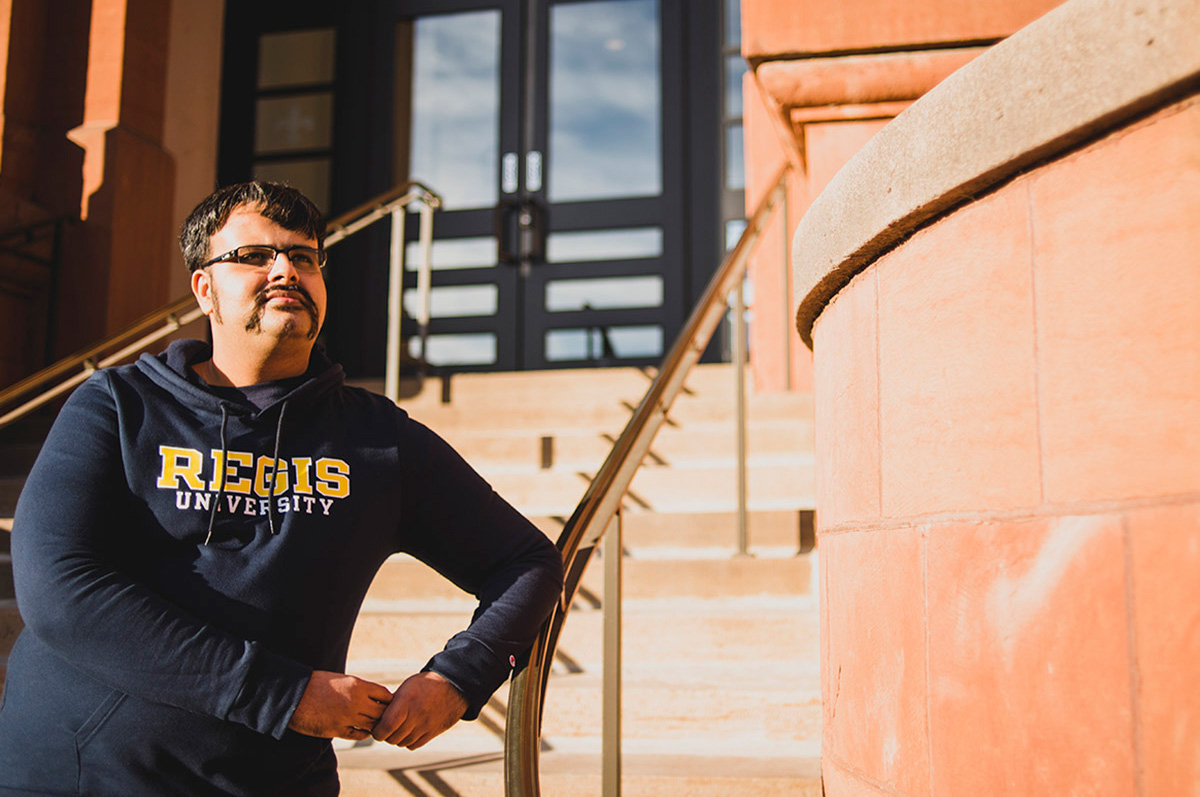 Sarvesh Karkhanis stands on the steps of Main Hall at Regis University's Northwest Denver Campus