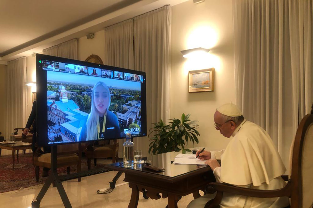 Pope Francis sits at a desk in his office across from a large screen displaying Keiry Sosa Velazquez 