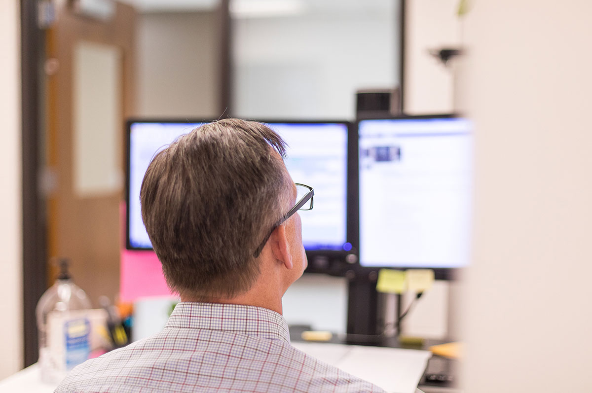 Man in professional clothing sits at a desk and looks at a computer in an office