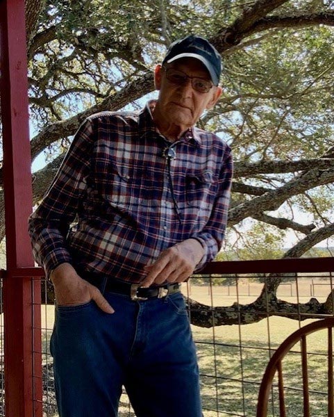 Ralph Dillon poses for a photo outside. Behind him are branches of a tree and a field