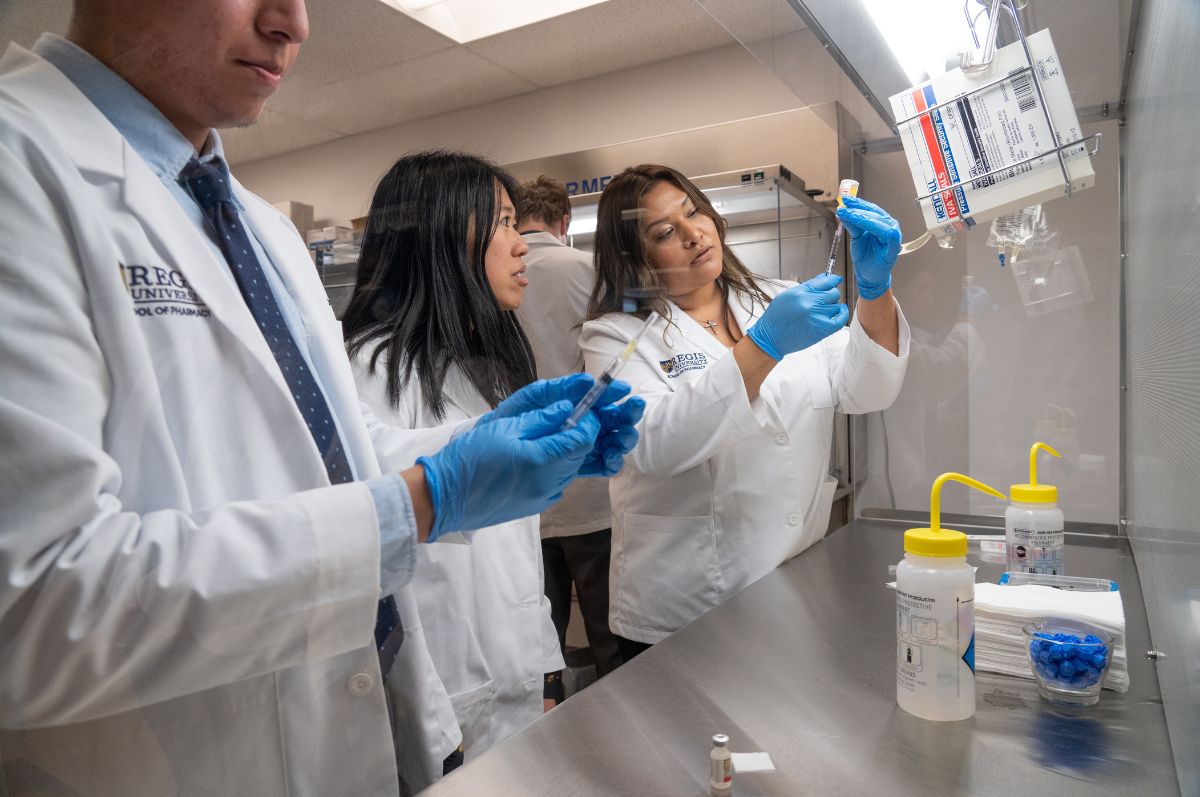 pharmacy faculty demonstrate how to administer medication while pharmacy students observe in the lab space