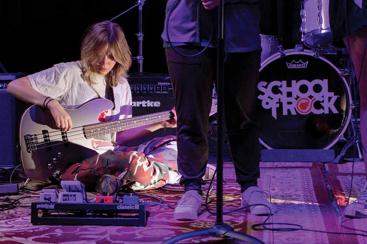 Student is sitting down on stage playing the bass