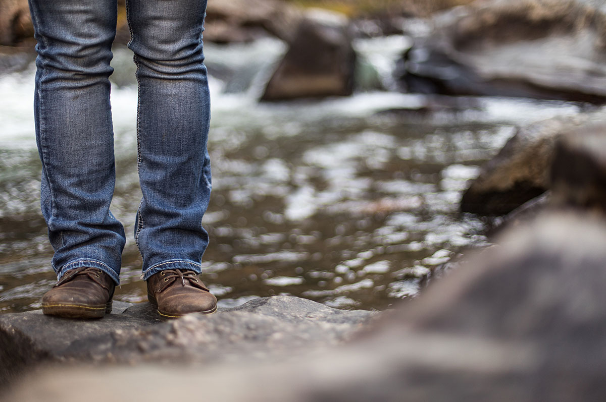 Legs stand on a boulder in the middle of a mountain stream