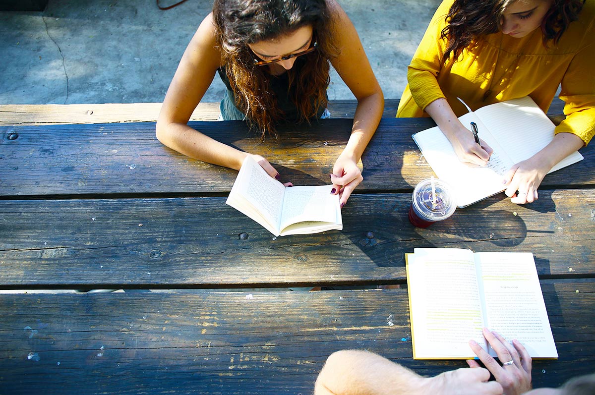 a group of students studies from books while sitting outside at a picnic table