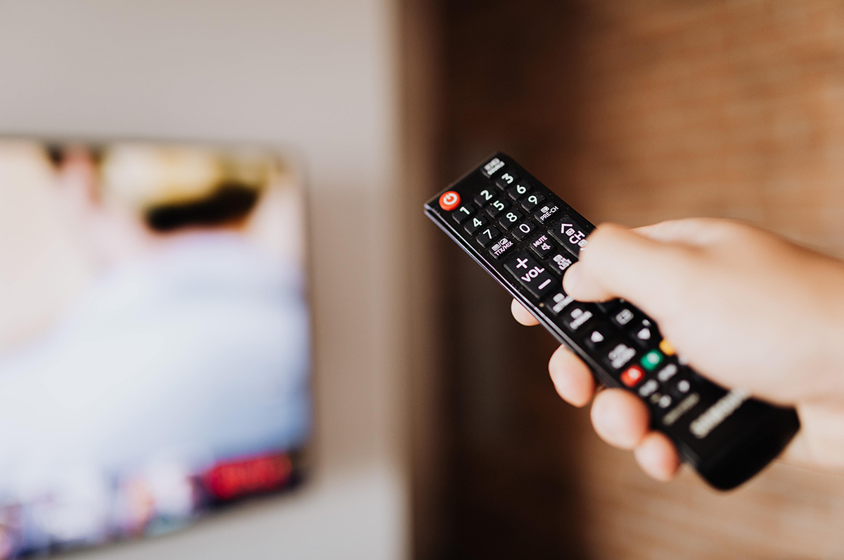 Person holding a remote watching advertisements on television