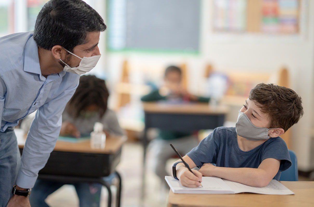 masked teacher working with student