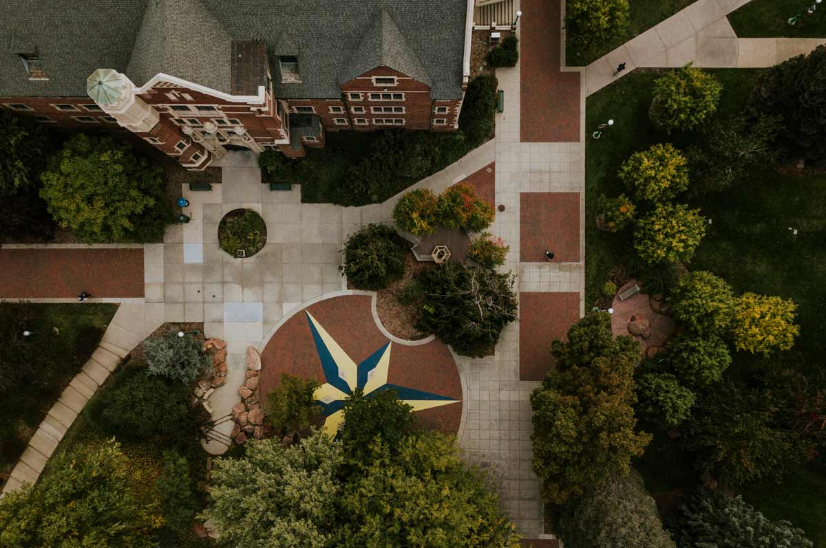 Top down aerial view of Regis campus featuring Carroll Hall on the top and the jesuit values compass on the bottom