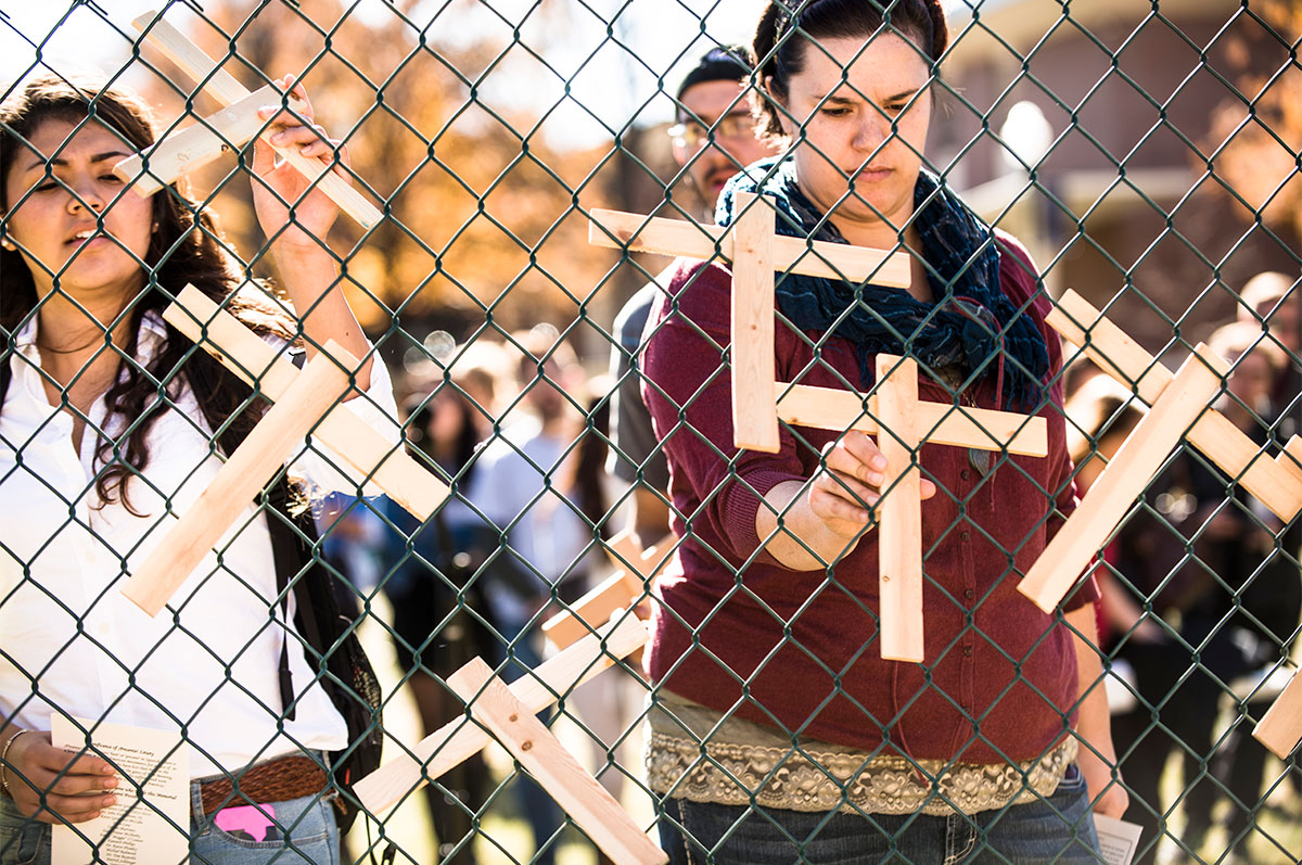 students hang wooden crosses on fence during memorial service