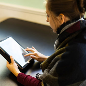 women sitting in a cafe intently reading on her tablet