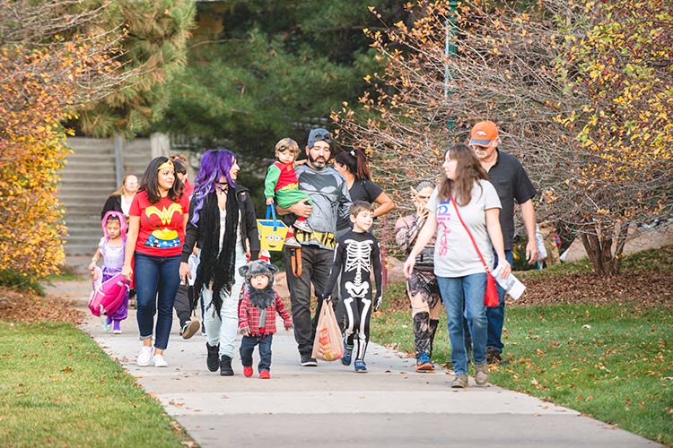 families dressed in Halloween costumes walk across the Quad with their treats in hand